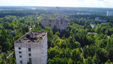 An aerial perspective reveals the haunting beauty of Pripyat, where nature relentlessly reclaims the abandoned Soviet-era buildings. Decades after the Chernobyl disaster, a dense forest engulfs the concrete structures, creating a powerful symbol of a post-apocalyptic world.の素材