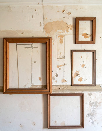 Empty wooden frames hang on a weathered, peeling wall, silent witnesses to forgotten stories. Each vacant space hints at a past life and lost memories, creating a poignant and nostalgic scene of abandonment and the beautiful decay of time.の素材