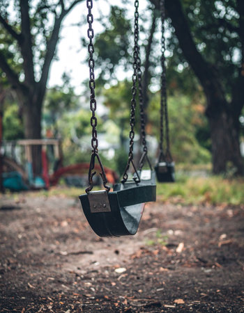 An empty swing hangs silently in a quiet park, its chains still. The scene evokes a sense of nostalgia and forgotten childhood memories, a poignant reminder of playtime and the passage of time.の素材