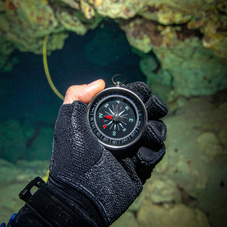 A cave divers gloved hand holds a compass steady, its needle a vital guide in the dark, mysterious depths of an underwater cavern. This first-person perspective captures the intense focus and courage required for exploration, navigating the unknown one decision at a time.の素材