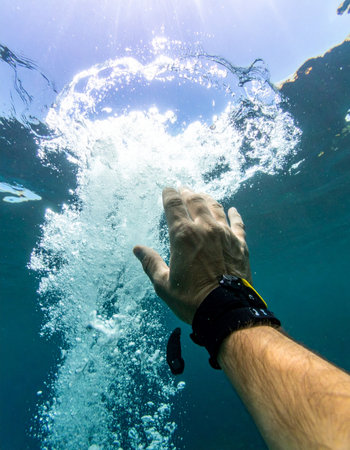 From the quiet depths, a hand reaches upward, breaking through the waters surface towards the life-giving light. This first-person perspective captures a powerful moment of struggle, hope, and the final push for freedom or survival. It symbolizes overcoming challenges and emerging into a new beginning.の素材