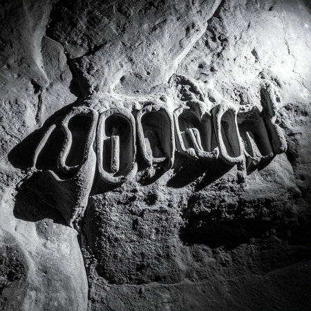 Deep within the earth, dramatic light reveals a mysterious inscription carved into the stone wall of a dark cave. This ancient art tells a forgotten story, a cryptic message from a lost civilization waiting to be deciphered by a modern explorer.の素材