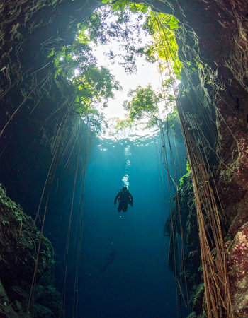 A lone freediver ascends through the crystal-clear, deep blue waters of a sacred cenote. A brilliant sunbeam penetrates the darkness from the jungle canopy above, illuminating the path to the surface and creating a moment of serene, breathtaking beauty and quiet adventure.の素材