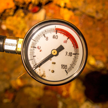 A close-up view captures the critical moment as a pressure gauges needle enters the red danger zone. This image symbolizes immense stress, system overload, and the brink of a critical failure, perfect for illustrating concepts of risk, deadlines, and industrial safety.の素材
