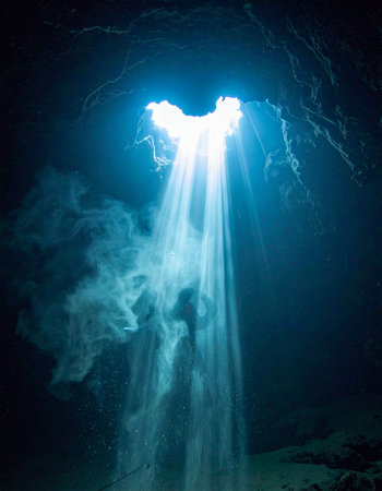 A brilliant, ethereal beam of blue light cuts through the darkness of a mysterious underground cave. Swirls of mist dance in the divine rays, creating a sense of wonder, hope, and spiritual discovery in the silent, sacred space.の素材