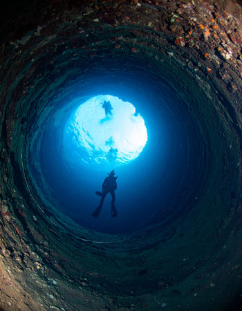 From the mysterious depths of a submerged cavern, a lone scuba diver begins the ascent toward the brilliant blue light of the surface. This image captures the thrilling moment of discovery and the profound sense of adventure found in exploring the hidden wonders of the underwater world.の素材