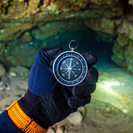 An explorer, deep within an underground grotto, consults their compass for guidance. The clear, turquoise water reflects the dim light, creating an atmosphere of mystery and discovery. This moment captures the essence of adventure, relying on classic tools to navigate an unknown world and find the right path.の素材