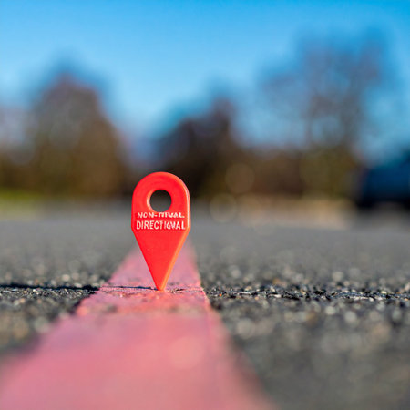 A single red location marker stands firmly on a painted line, pointing the way forward on an open road. This image symbolizes clarity, purpose, and the start of a journey towards a specific goal or destination, with a clear path to follow.の素材