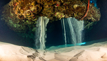A stunning and rare view of a deep-sea brine pool, where super-saline water, denser than the surrounding ocean, cascades like an otherworldly waterfall over a rocky ledge onto the sandy seabed. This mysterious natural phenomenon highlights the extreme and alien environments that exist in the unexplored frontiers of our planets oceans.の素材