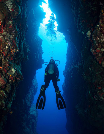 A lone scuba diver ventures into the silent, deep blue world of a narrow underwater canyon. Sunlight filters from above, illuminating the path forward on an incredible journey of exploration and discovery into the unknown.の素材