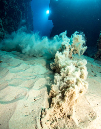 In the silent, crushing depths of the ocean, a geothermal vent releases a plume of superheated minerals, offering a rare glimpse into the planets powerful geological activity. This dramatic eruption on the sandy seabed highlights the extreme environments that exist far below the surface.の素材