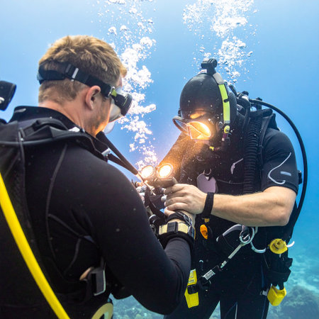 In the quiet depths of the ocean, a team of two professional commercial divers collaborates on a critical task. One welder carefully applies a torch, creating a brilliant flash of light and sparks, while his partner assists, showcasing precision, skill, and teamwork in a challenging underwater environment.の素材