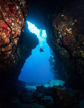 A lone scuba diver is silhouetted against the brilliant blue light at the entrance of a dark, mysterious underwater cave. This image captures the spirit of adventure and the serene beauty of exploring the hidden depths of the ocean, inviting the viewer into a world of quiet wonder and discovery.の素材