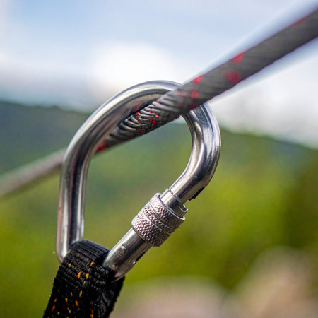 A close-up view of a sturdy metal carabiner, its screw gate securely fastened. A climbing rope runs through it, representing a vital connection and the essence of safety and trust in outdoor adventure sports against a backdrop of rugged mountains.の素材