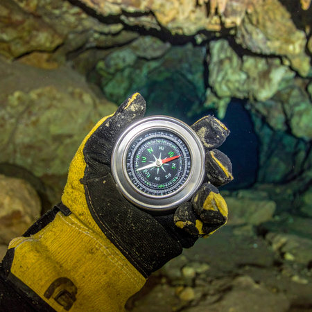 Deep within the earth, an explorer relies on a trusty compass to navigate the labyrinthine passages of a dark cave. The needle points the way forward, a symbol of guidance and hope in the face of the unknown on a thrilling underground adventure.の素材