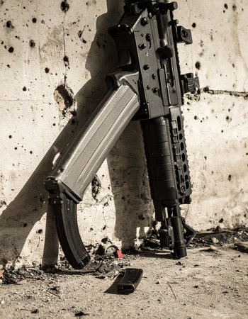 A modern assault rifle rests against a bullet-scarred concrete wall, a silent testament to a recent and intense firefight. The surrounding debris and pockmarks tell a story of conflict, power, and survival in a high-stakes environment.の素材