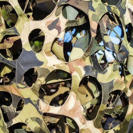 A detailed view of a tactical camouflage net, its intricate die-cut pattern designed for ultimate concealment. The overlapping layers of earthy tones create a complex texture, perfect for backgrounds related to military operations, hunting, survival, or abstract design concepts.の素材
