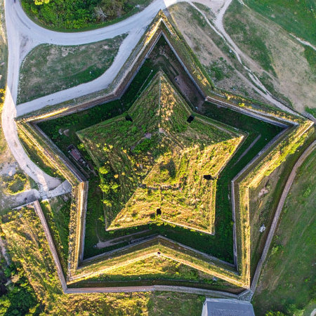 The suns golden light casts long shadows across the ancient earthworks of a star-shaped fortress. This aerial perspective reveals the intricate geometric design, a testament to historical military strategy and architectural ingenuity, standing as a silent monument to a bygone era.の素材