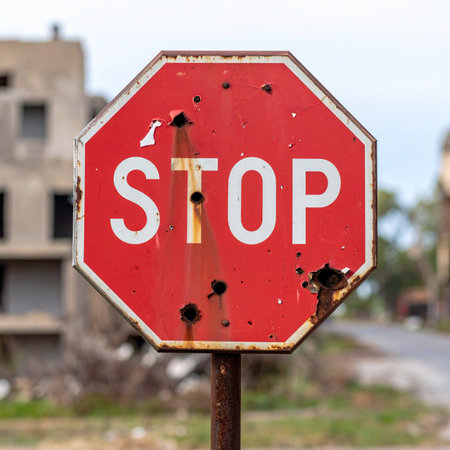 A weathered stop sign, pierced by bullet holes, stands as a silent witness in a desolate, war-torn landscape. Its message of order is defied by the visible scars of conflict and chaos, symbolizing a breakdown of society and the lingering presence of danger.の素材