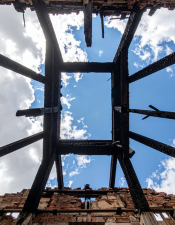 From the ashes of a forgotten building, the skeletal remains of a burnt roof frame a perfect view of the bright blue sky. A powerful symbol of resilience, new beginnings, and hope emerging from destruction and decay.の素材