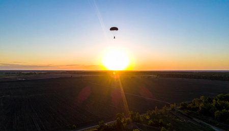 A lone skydiver makes a final descent, silhouetted against the brilliant glow of a setting sun. This aerial perspective captures a moment of pure freedom and serene adventure, high above a vast and empty landscape, embodying courage and the thrill of exploration.の素材