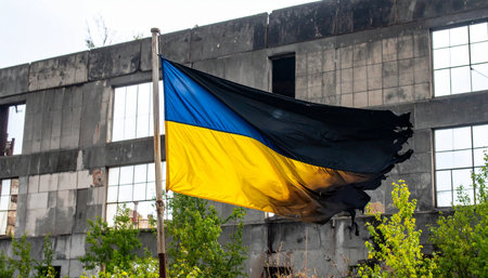 A tattered yet proud Ukrainian flag waves defiantly in the wind, a powerful symbol of national resilience and enduring hope set against the stark backdrop of a war-damaged building. This poignant image captures the spirit of survival and the unyielding fight for freedom amidst the devastation of conflict.の素材