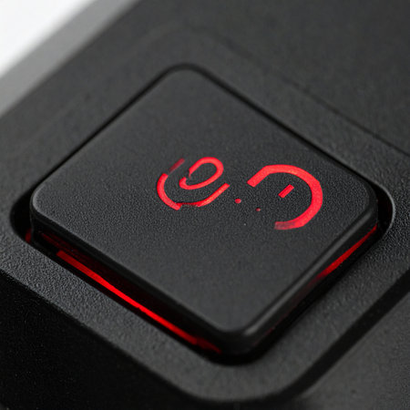 A macro close-up of a single black button, its red symbol glowing intensely in the dark.の素材