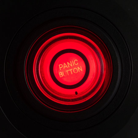 A close-up of a glowing red panic button on a dark control panel.の素材