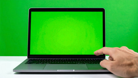 A user's hand reaches out to interact with a laptop featuring a green chroma key screen.の素材