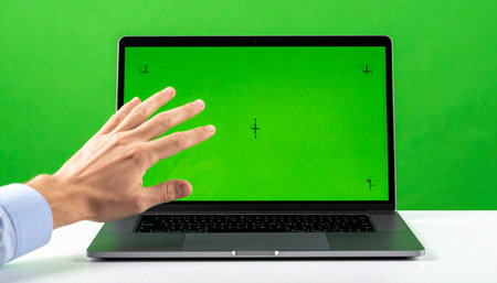 A developer's hand gestures towards a laptop with a green screen, ready for custom content.の素材