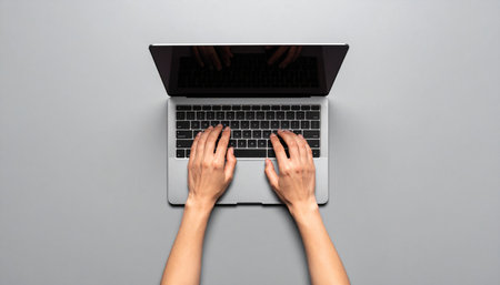From a bird's-eye view, a person's hands are busy at work, typing on a sleek laptop.の素材