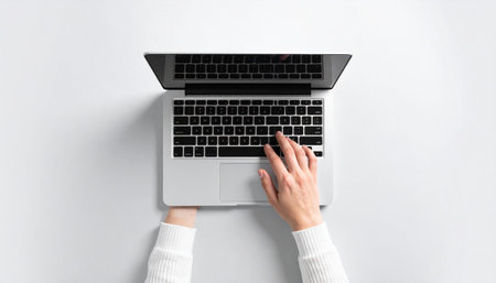 From a top-down perspective, a professional's hands move swiftly across a laptop keyboard, set against a clean, white background.の素材