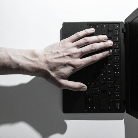 In a minimalist, high-contrast setting, a hand rests poised over a laptop keyboard.の素材