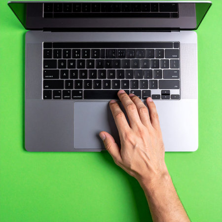 From a top-down perspective, a hand navigates a laptop on a vibrant green surface.の素材