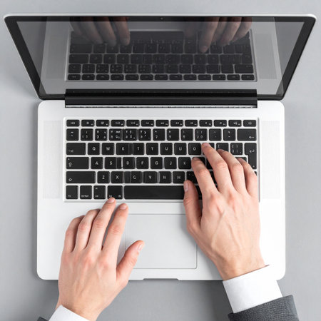 From an overhead perspective, a professional in a suit diligently types on a modern laptop.の素材