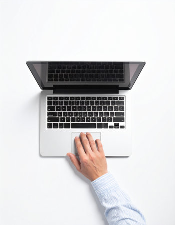 An overhead view captures a moment of focused productivity. A person's hand rests on the trackpad of a sleek, modern laptop, set against a clean white background.の素材