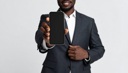 A confident African American businessman in a sharp suit proudly presents a smartphone with a blank screen.の素材