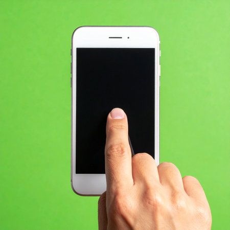 A close-up view of a finger tapping the blank screen of a modern smartphone, set against a vibrant green background.の素材