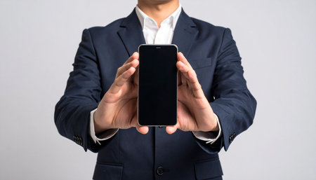 A confident executive in a sharp suit presents a new smartphone, its blank screen a canvas for innovative ideas, applications, or a crucial business message.の素材