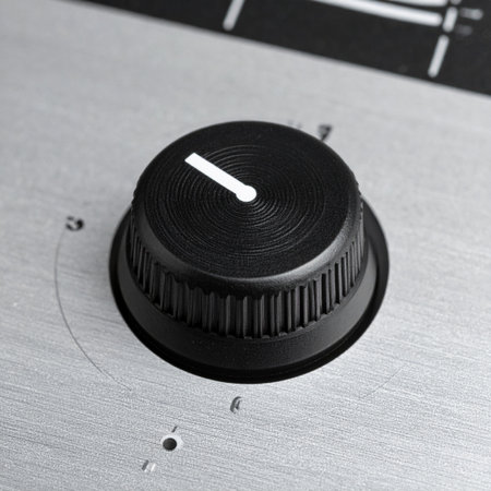 A detailed macro shot of a single black control knob on a brushed aluminum surface.の素材
