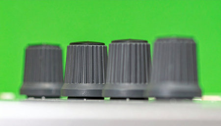 A close-up view of four black control knobs lined up on a piece of studio equipment.の素材