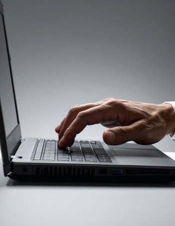 A professional's hand moves swiftly across the laptop keyboard, deep in concentration.の素材