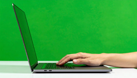 Side view of a person's hand on a modern laptop, poised over the trackpad. The vibrant green screen is ready for custom content, perfect for mockups, tutorials, or visual effects projects.の素材