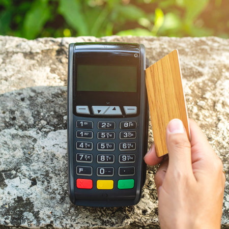 A person makes a quick and secure tap-to-pay transaction with a unique wooden credit card at a POS terminal.の素材