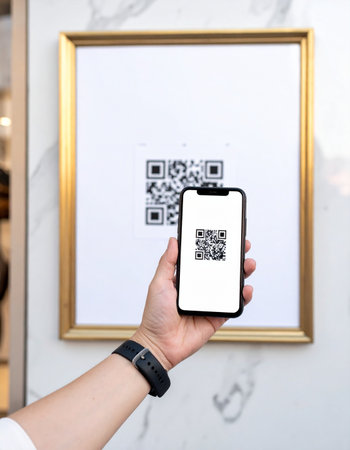 A person holds a smartphone to scan a QR code displayed in a gold frame, instantly accessing digital information.の素材