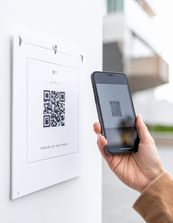 A person uses their smartphone to scan a QR code on a wall sign, instantly accessing digital information.の素材