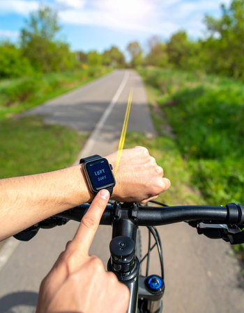 From a first-person perspective, a cyclist checks their workout progress on a smartwatch.の素材