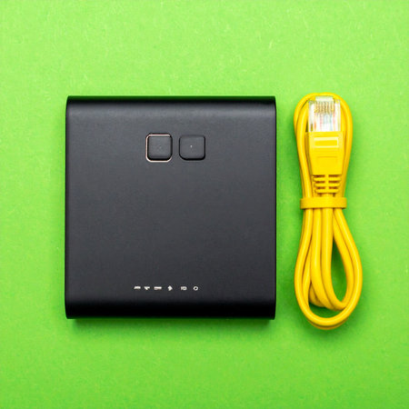 A top-down view of essential networking equipment, a sleek black router and a bright yellow ethernet cable, neatly arranged on a vibrant green background.の素材