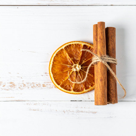 A bundle of fragrant cinnamon sticks tied with rustic twine rests beside a translucent slice of dried orange.の素材