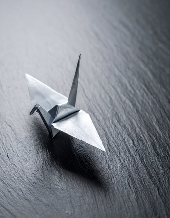 A single, elegant origami crane rests peacefully on a dark, textured slate surface.の素材
